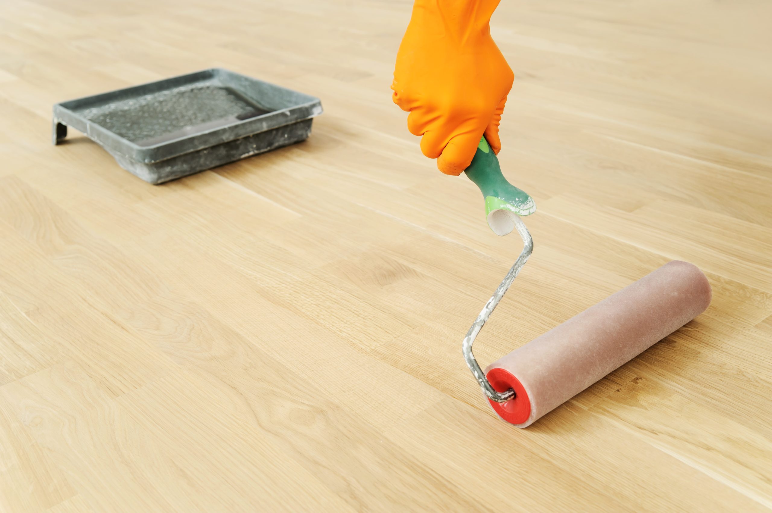 Close-up of a worker rolling clear lacquer onto a freshly sanded oak hardwood floor during Wood Floor Sanding in a South Woodford home.