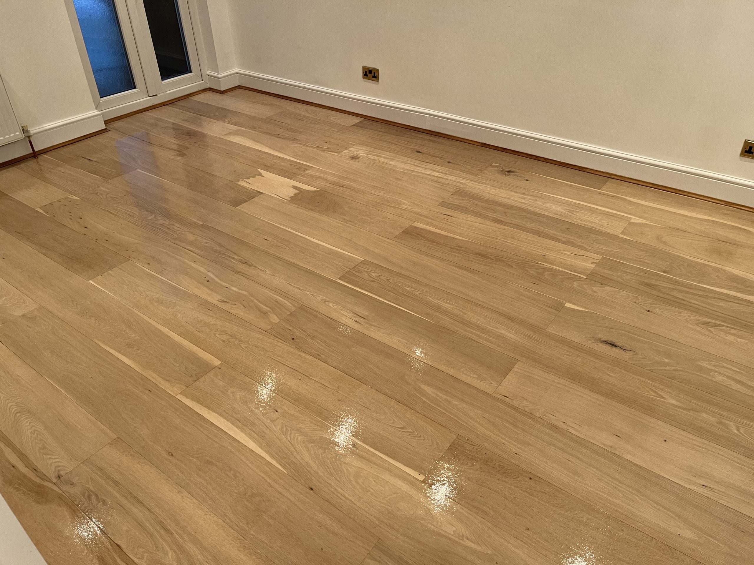Newly finished oak plank hardwood floor gleaming after professional Wood Floor Sanding in a South Woodford living room.