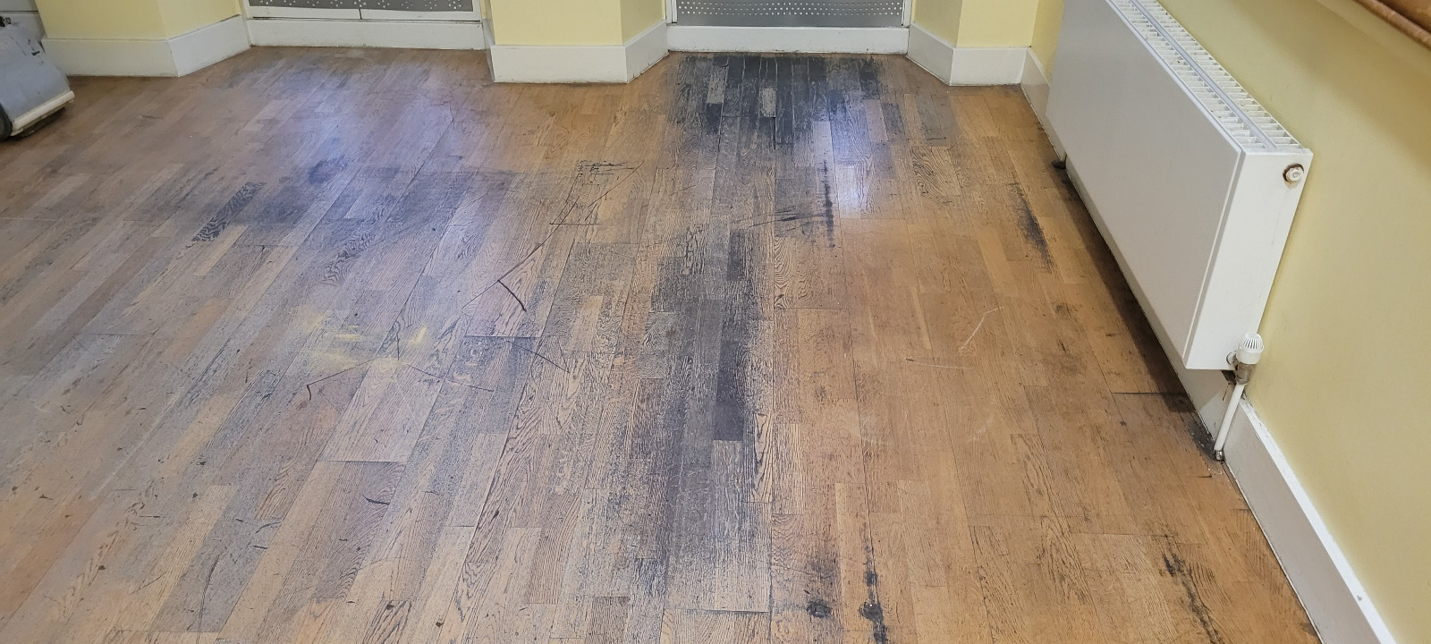 Heavily scuffed oak strip hardwood floorboards inside a South Woodford room awaiting professional Wood Floor Sanding.