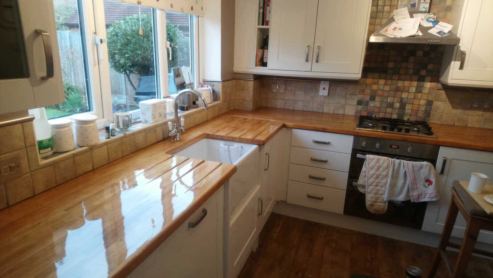 Freshly completed Worktop Refinishing in southwoodford, showing glossy solid oak hardwood kitchen worktops and a matching oak hardwood floor in a bright U-shaped kitchen.