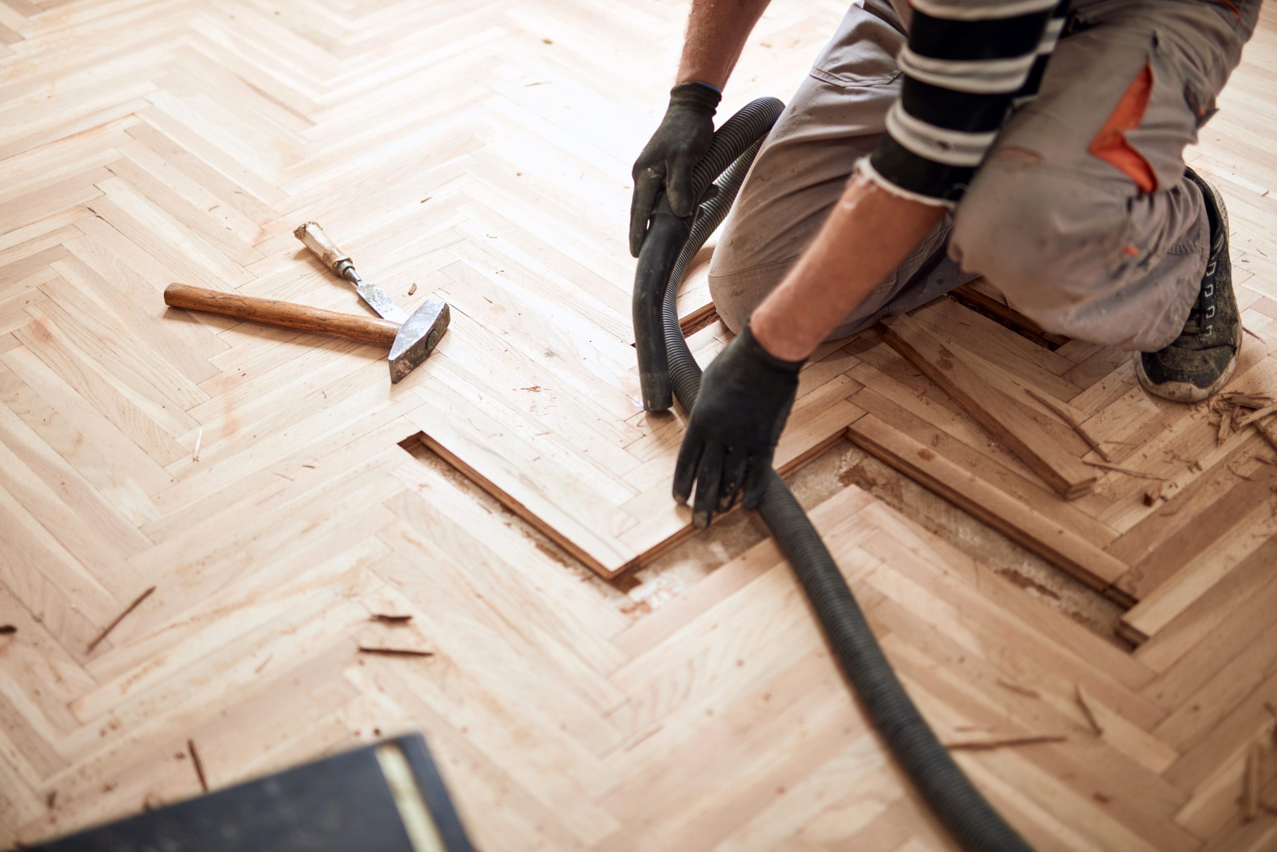 Wood Floor Sanding in Southwoodford with a technician repairing a light oak herringbone parquet wood floor, replacing damaged blocks before sanding and refinishing.