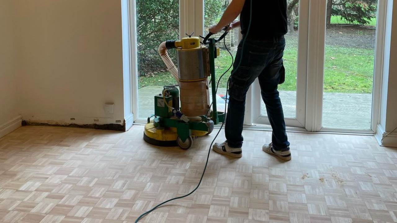 Wood Floor Sanding in Southwoodford on a light oak mosaic finger parquet wood block lounge floor, with a professional sanding machine working near patio doors.