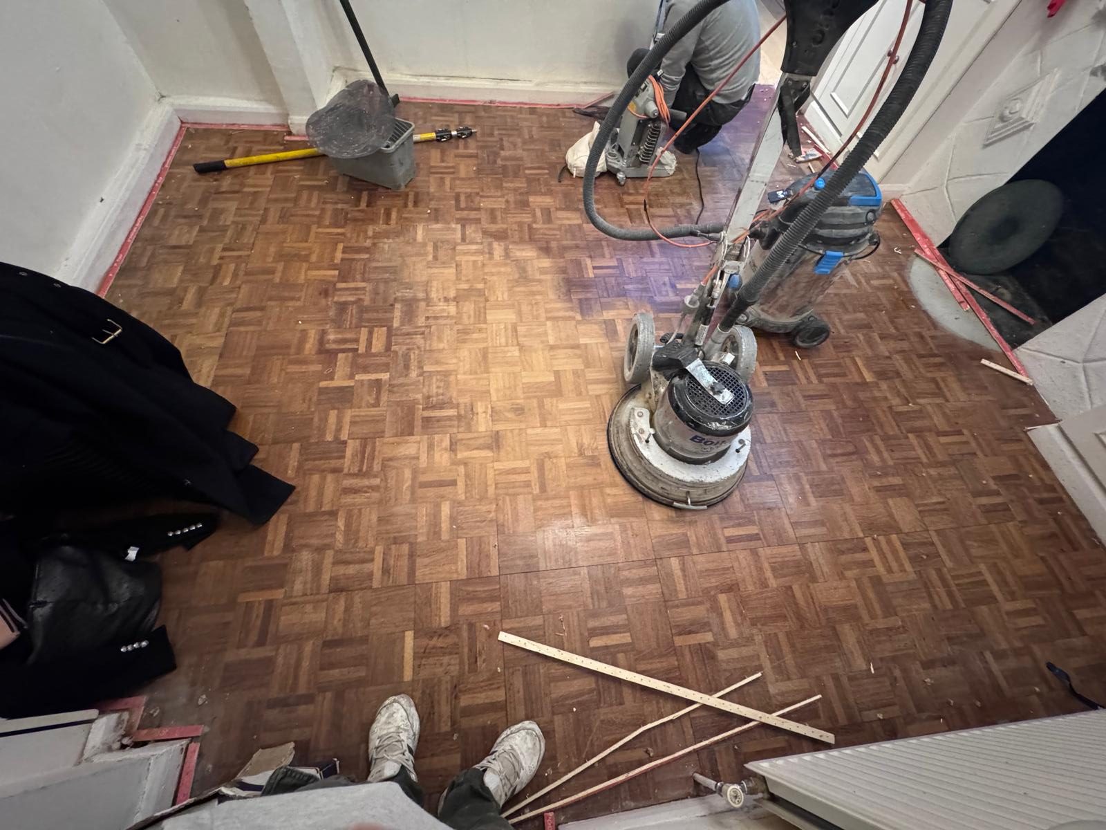 Wood Floor Sanding in Southwoodford in progress on an oak mosaic parquet wood block hallway floor, with professional sanding machine and dust extraction setup.