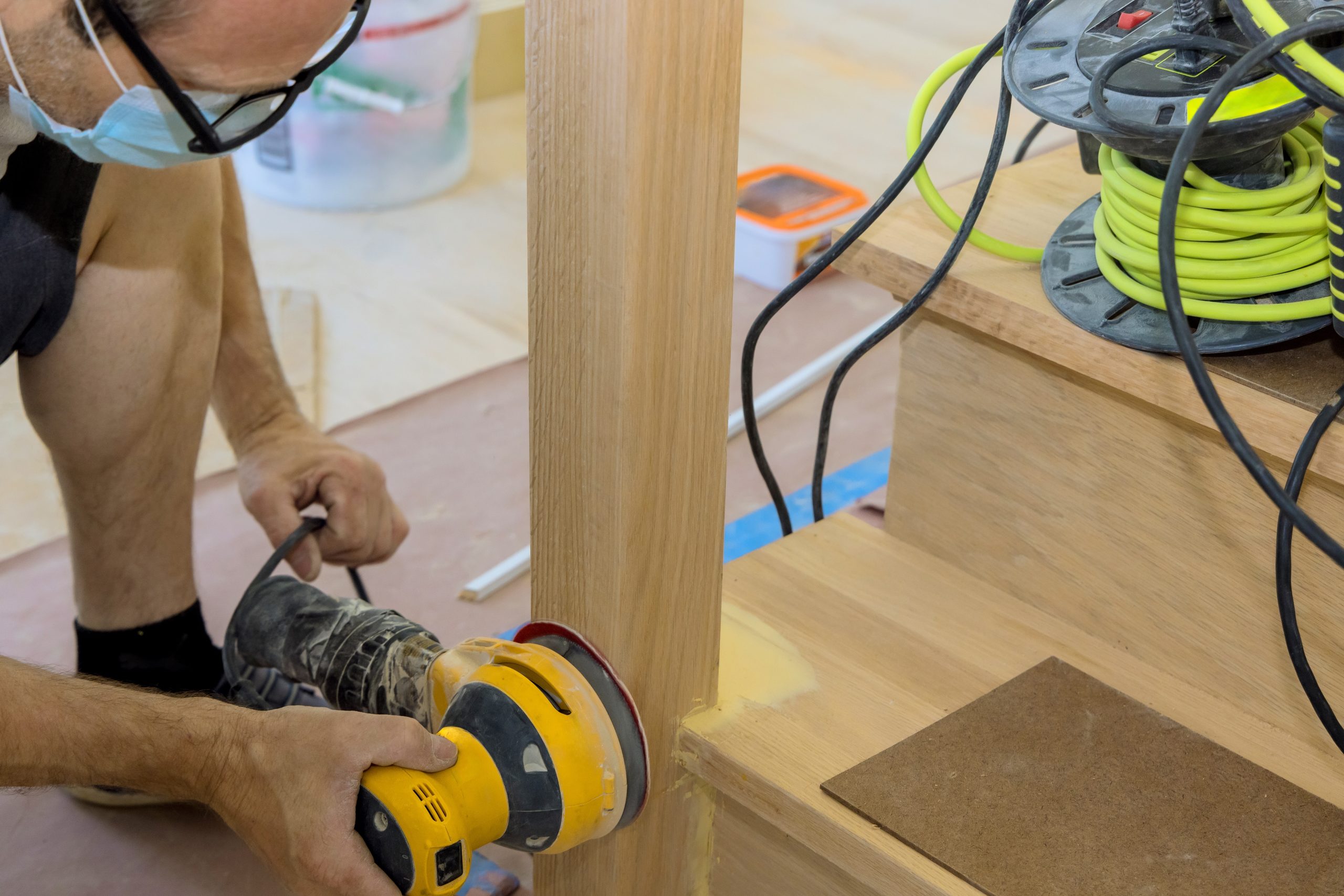 Wood Floor Sanding in Southwoodford showing a technician sanding a solid oak staircase tread and balustrade with an orbital sander for a smooth refinished surface.